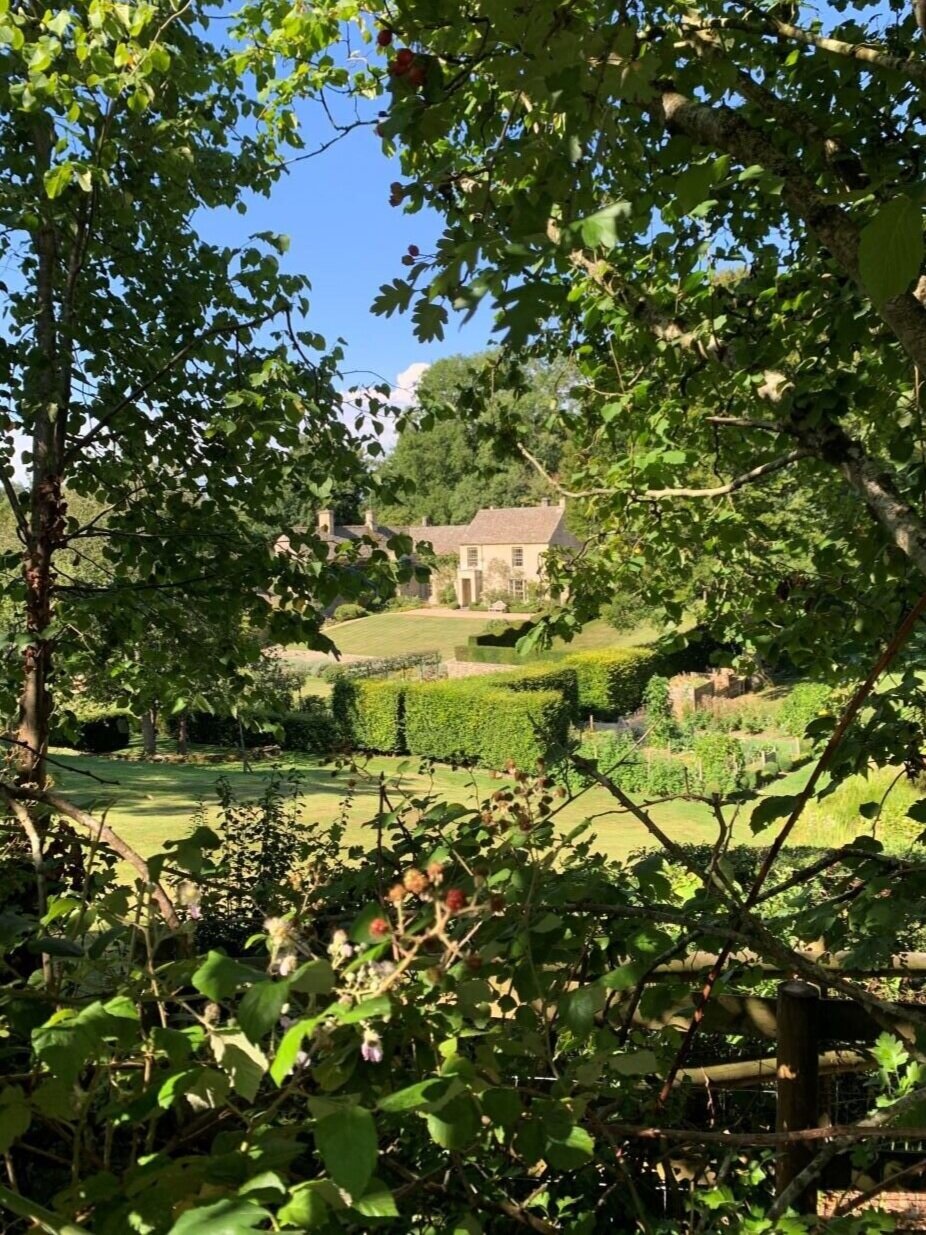 Cotswold stone farmhouse glimpsed through trees